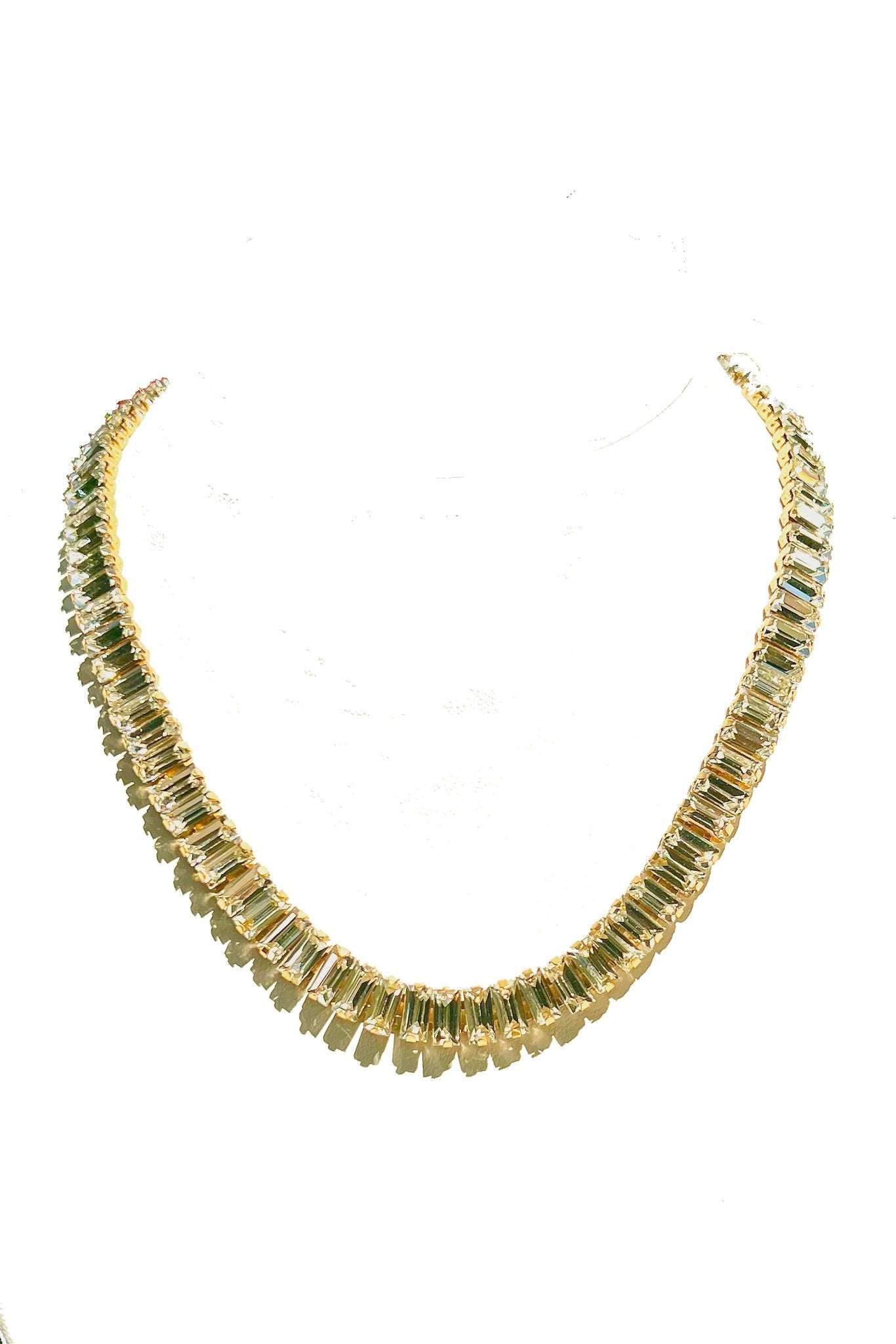 a gold necklace with green stones on a white background